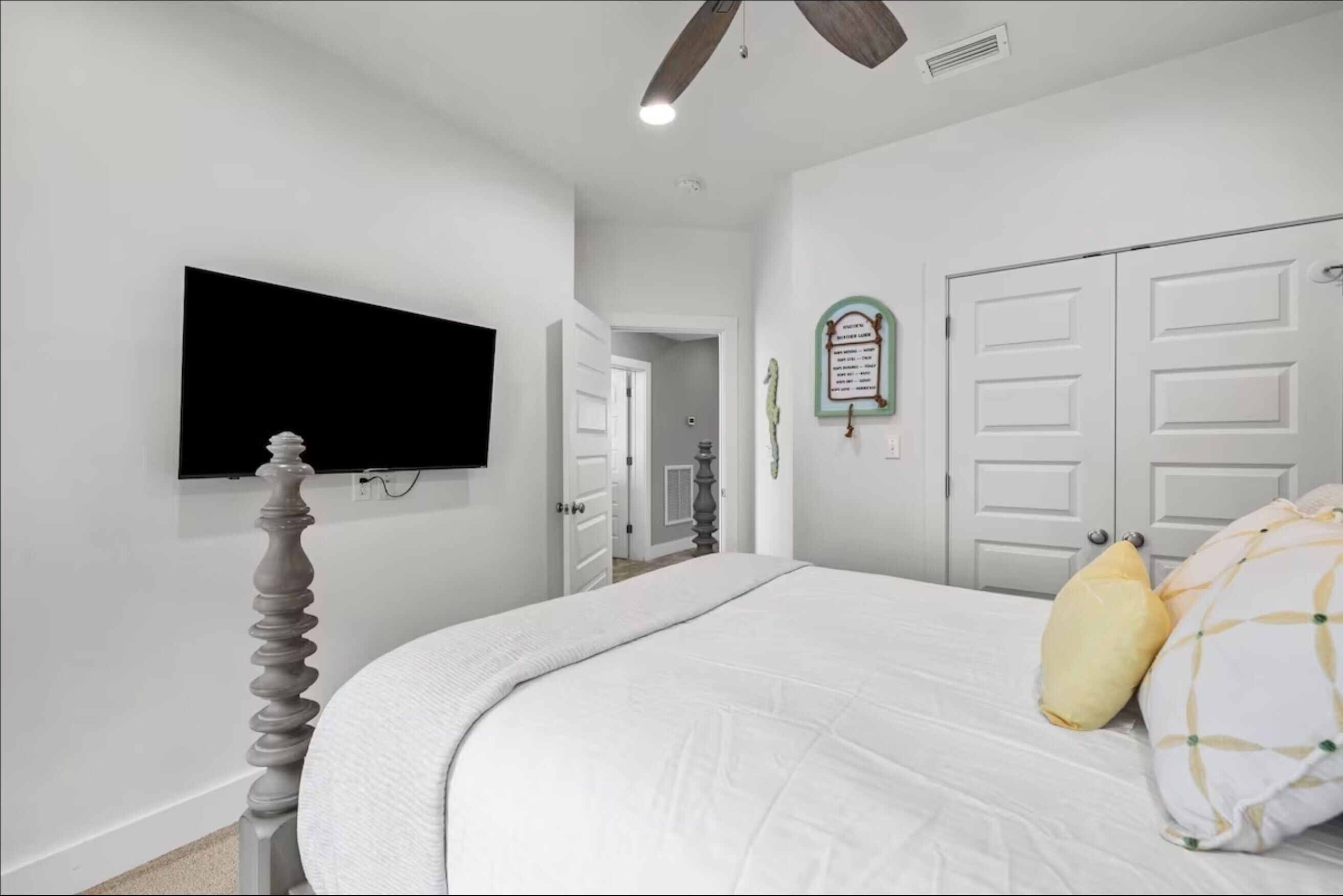 Een slaapkamer met een bed, een televisie aan de muur, een plafondventilator en een deur met een bordje.