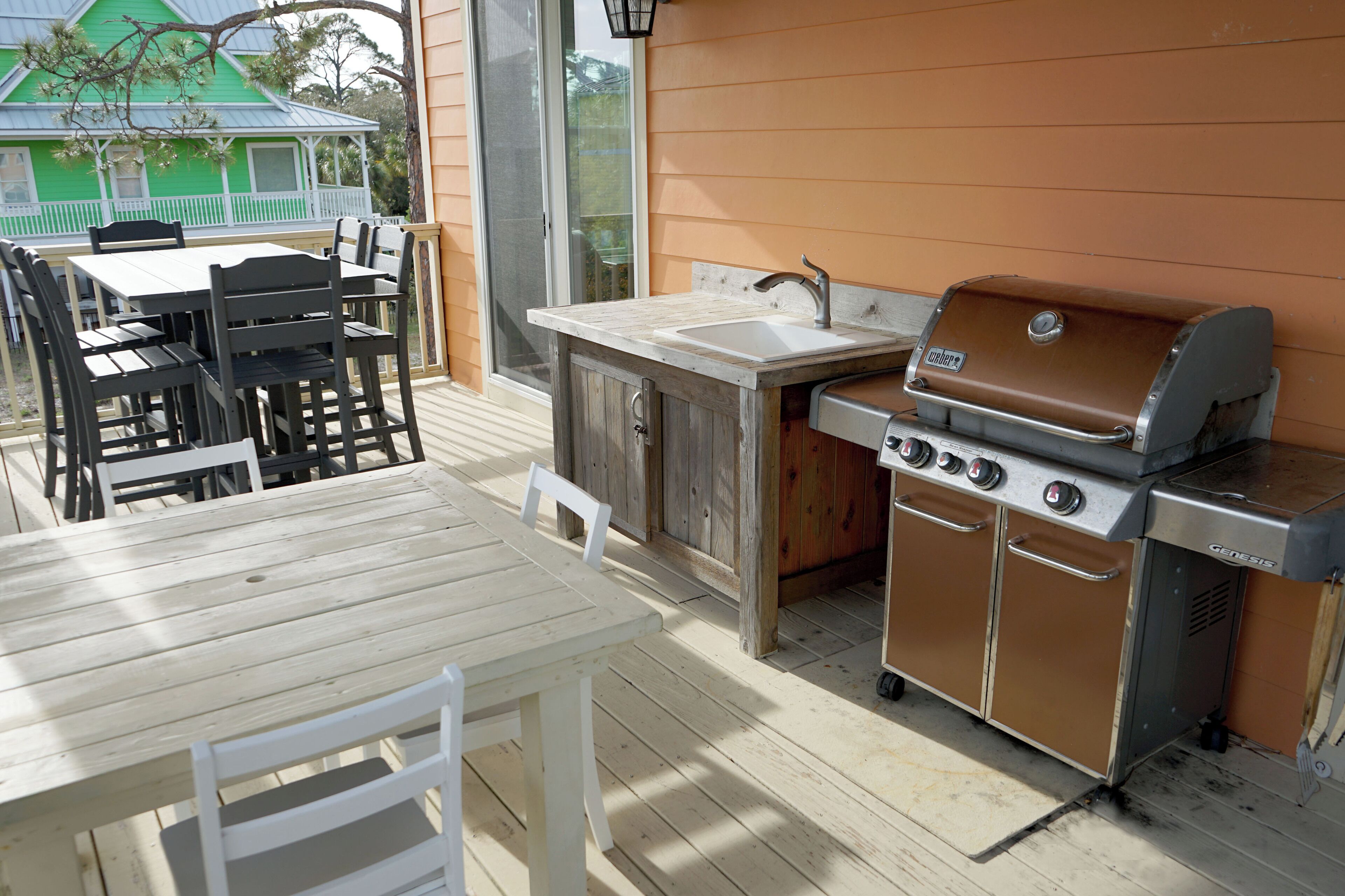 An outdoor kitchen with a grill, sink, and dining area with chairs and a table.