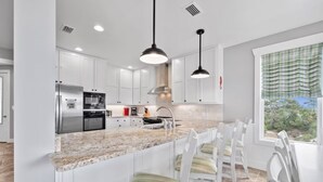 Cocina moderna con armarios blancos, encimera de granito e iluminación colgante.