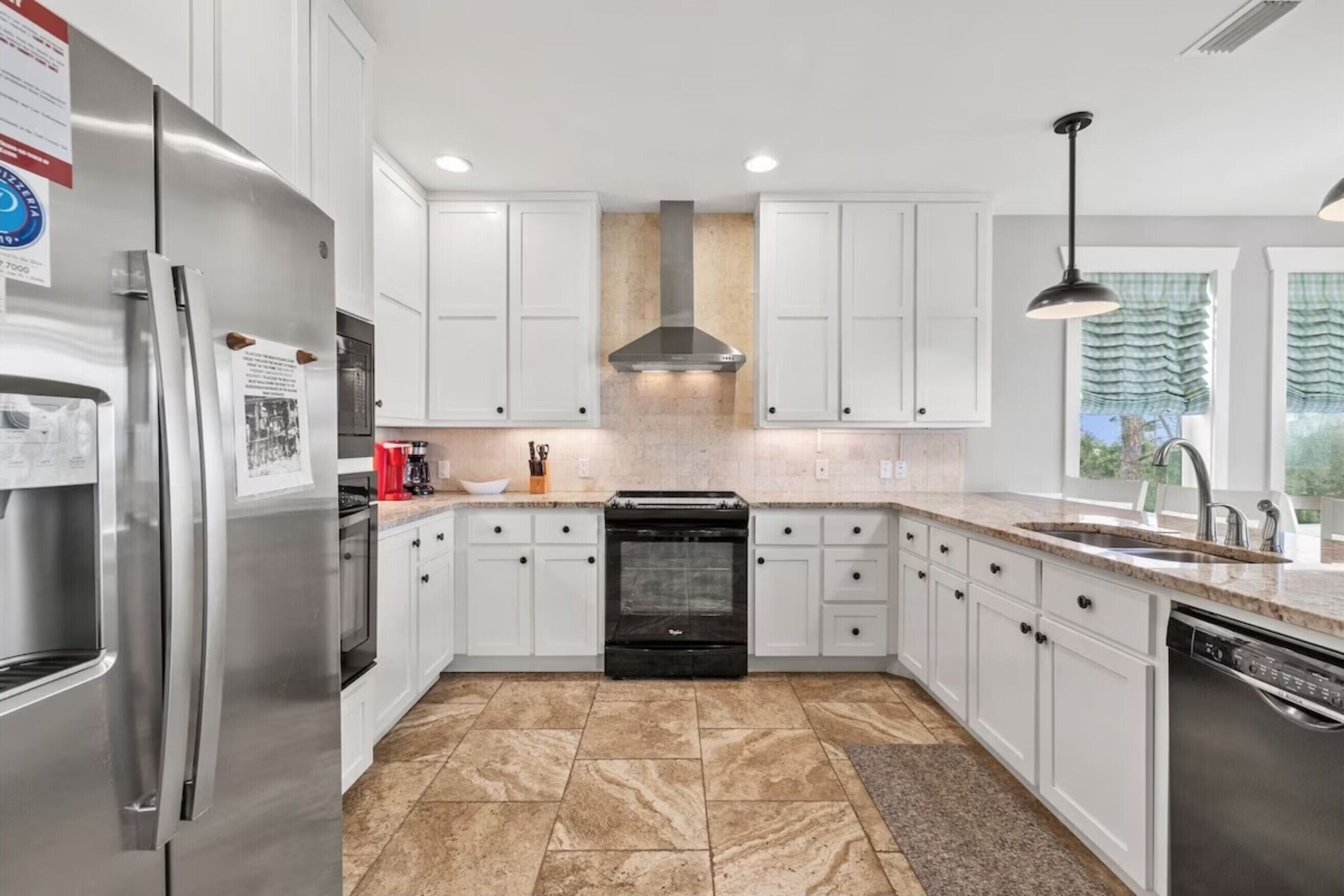 A modern kitchen with white cabinets, a stainless steel refrigerator, a built-in oven, and a large window with a view.