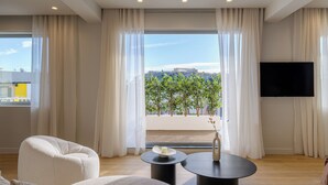 A modern living room with a large window, a flat-screen TV, and a view of a building and trees. - Acropolis Penthouse Plunge Pool (Athina)