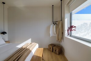 A bedroom with a bed, bedside table, hanging clothes rack, window with view, and two wicker baskets. - Acropolis Penthouse Plunge Pool (Athina)
