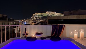 A rooftop terrace with a view of the Acropolis at night, a hot tub, candles, and a bowl of grapes. - Acropolis Penthouse Plunge Pool (Athina)
