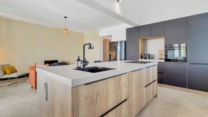 Una cocina moderna con una isla central, muebles oscuros y una lámpara colgante.