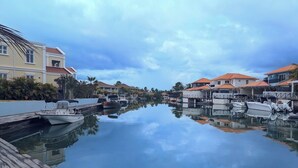 Una marina con barcos amarrados, un muelle de madera y casas con tejados rojos al fondo.
