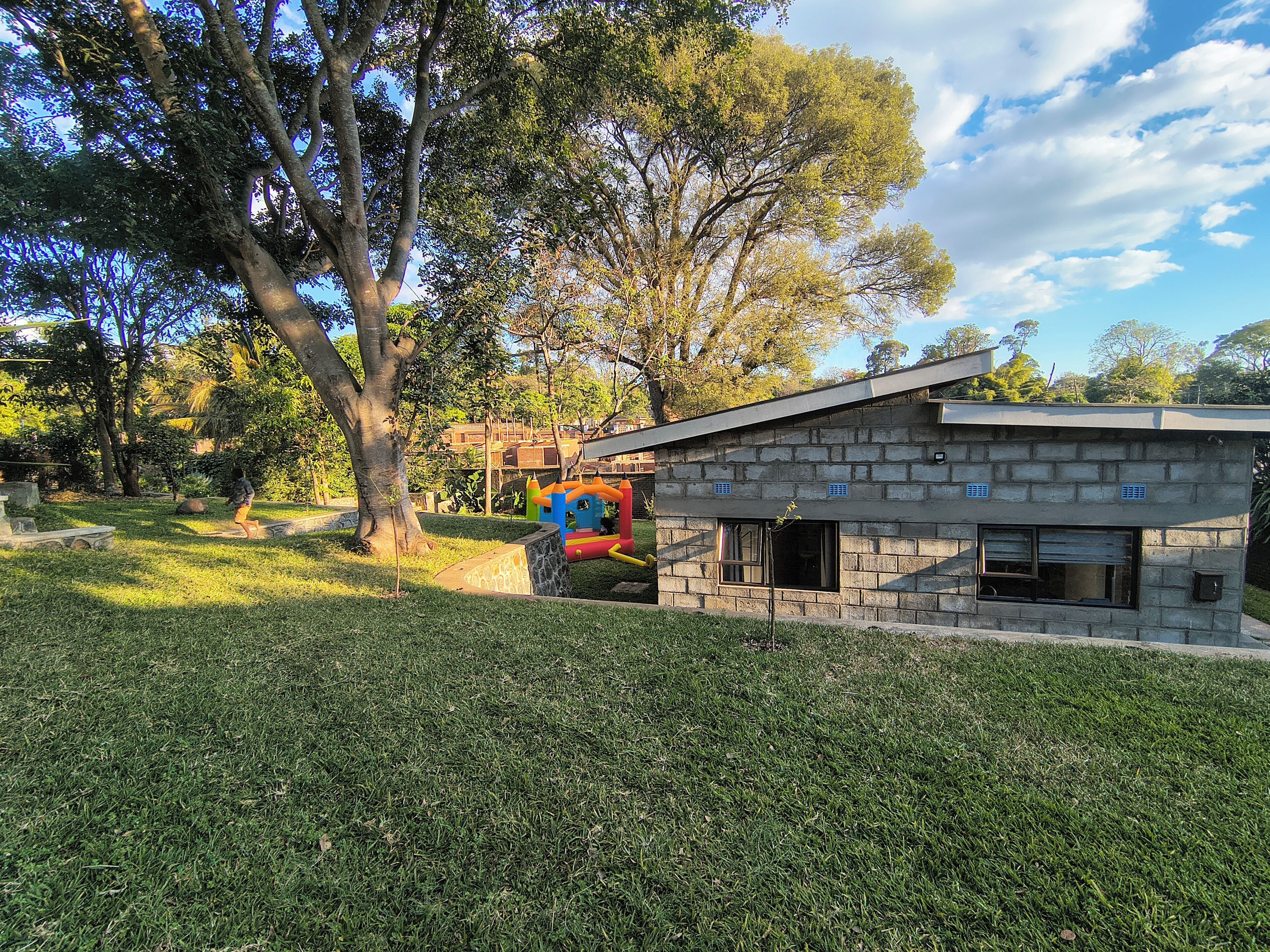 A stone building with a window and a door, surrounded by grass and trees.
