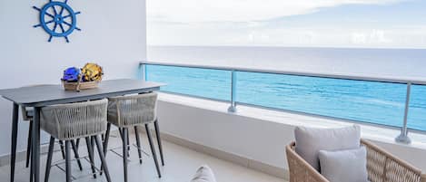 A balcony with a view of the ocean, a table with chairs, and a wicker chair.