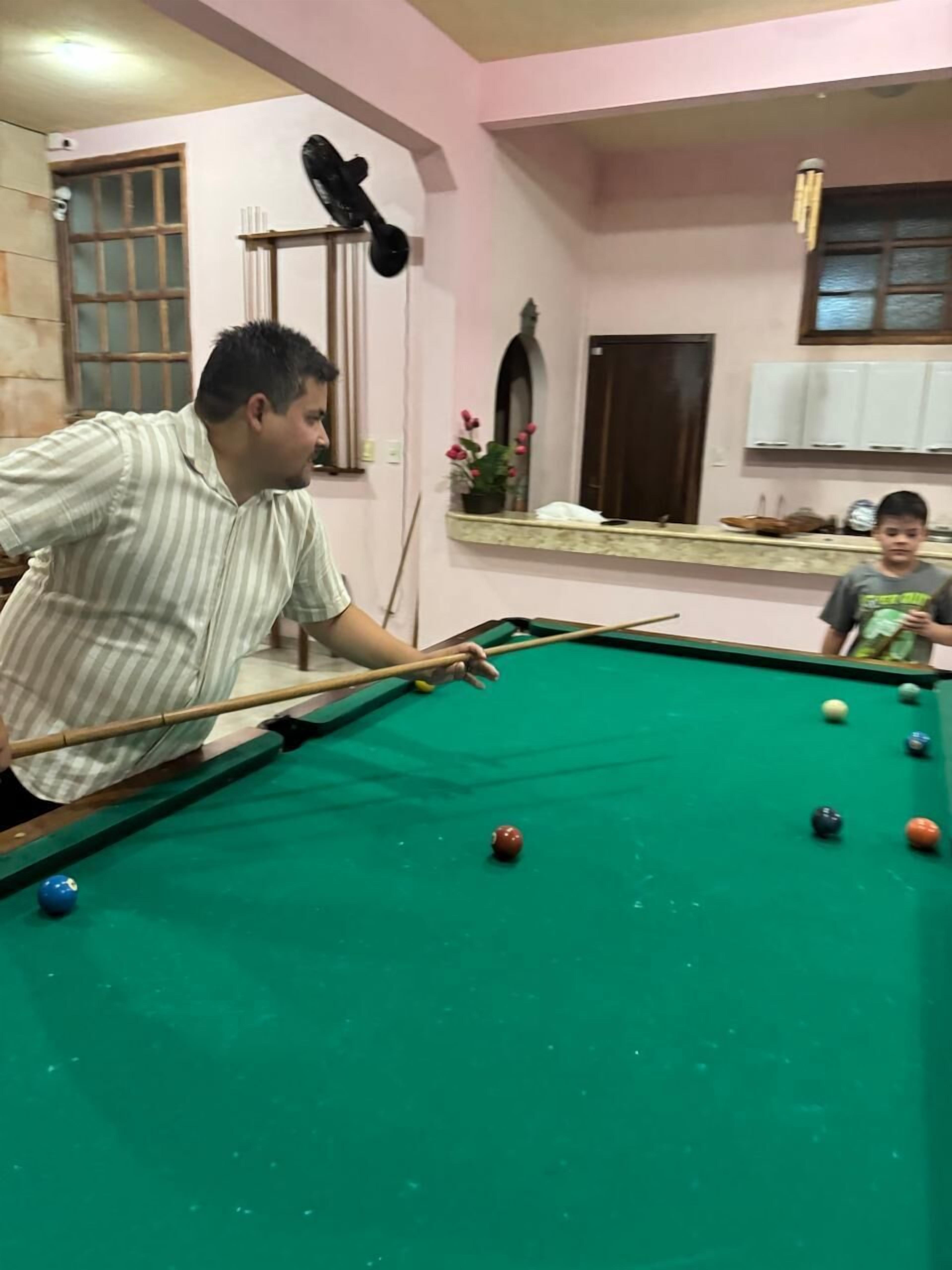 A pool table with balls in a room with pink walls, a window, and a cabinet.
