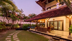 A house with a tiled roof, a covered patio with seating, and a well-maintained lawn with patterned stepping stones. - Villa Panda Seminyak Next to KU DE TA (Seminyak)