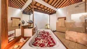 A bathroom with a bathtub filled with rose petals, wooden beams on the ceiling, and a large mirror. - Villa Panda Seminyak Next to KU DE TA (Seminyak)