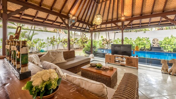 A covered outdoor seating area with a pool, wicker furniture, and a television. - Villa Panda Seminyak Next to KU DE TA (Seminyak)