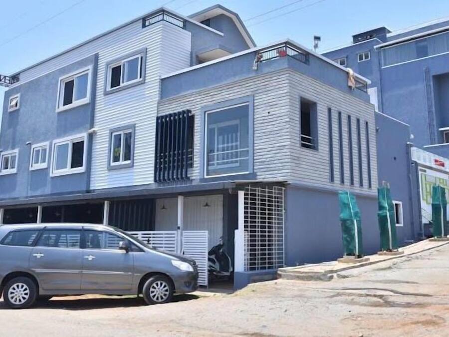 Um edifício de dois andares com uma garagem, um carro estacionado em frente e uma pessoa perto da entrada.