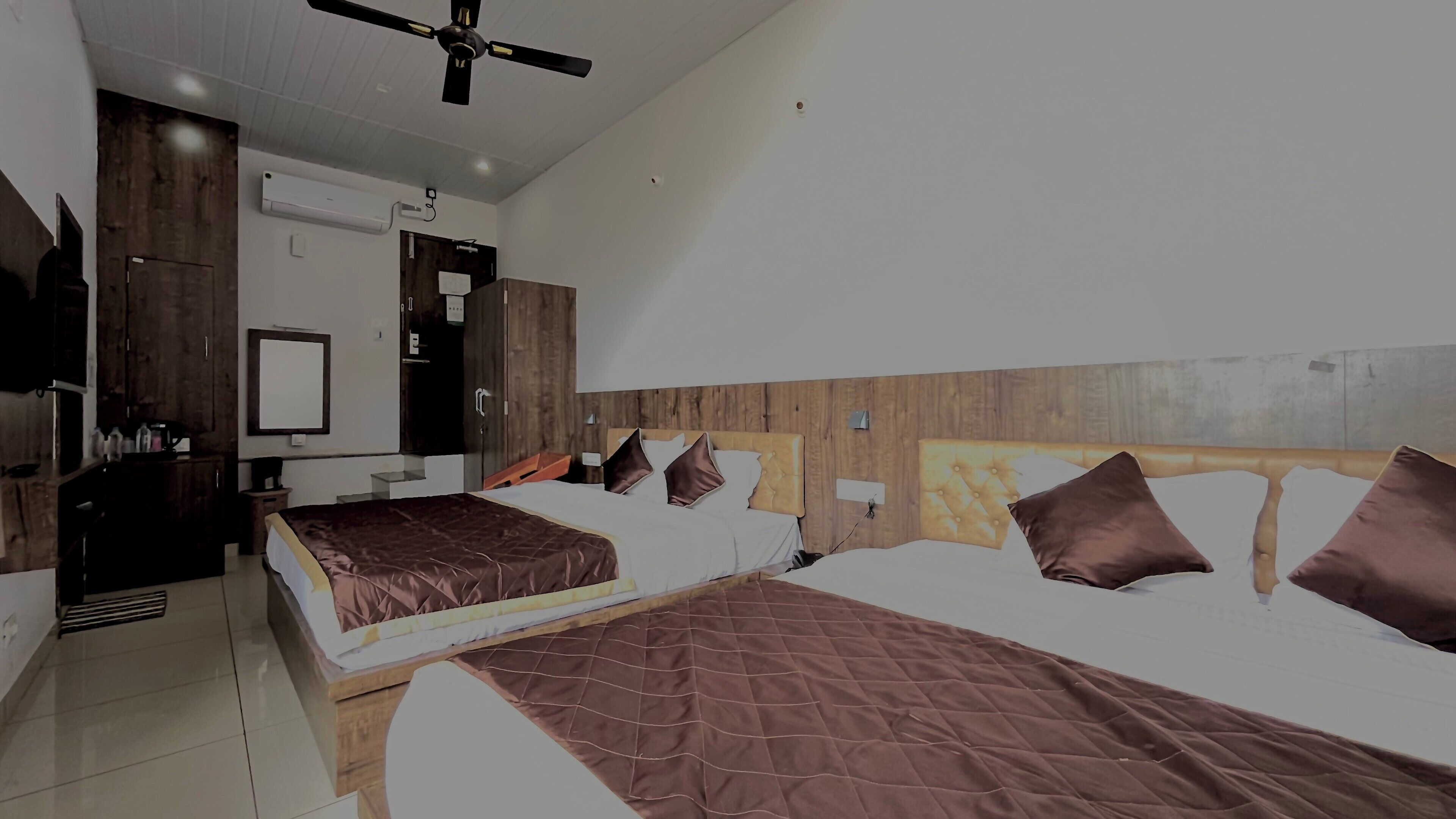 Een hotelkamer met twee bedden, een plafondventilator, een houten hoofdbord en een klein bureau met een stoel.
