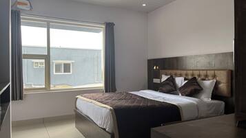 A hotel room with a large bed, a bedside table, a window with curtains, and a view of a building outside.