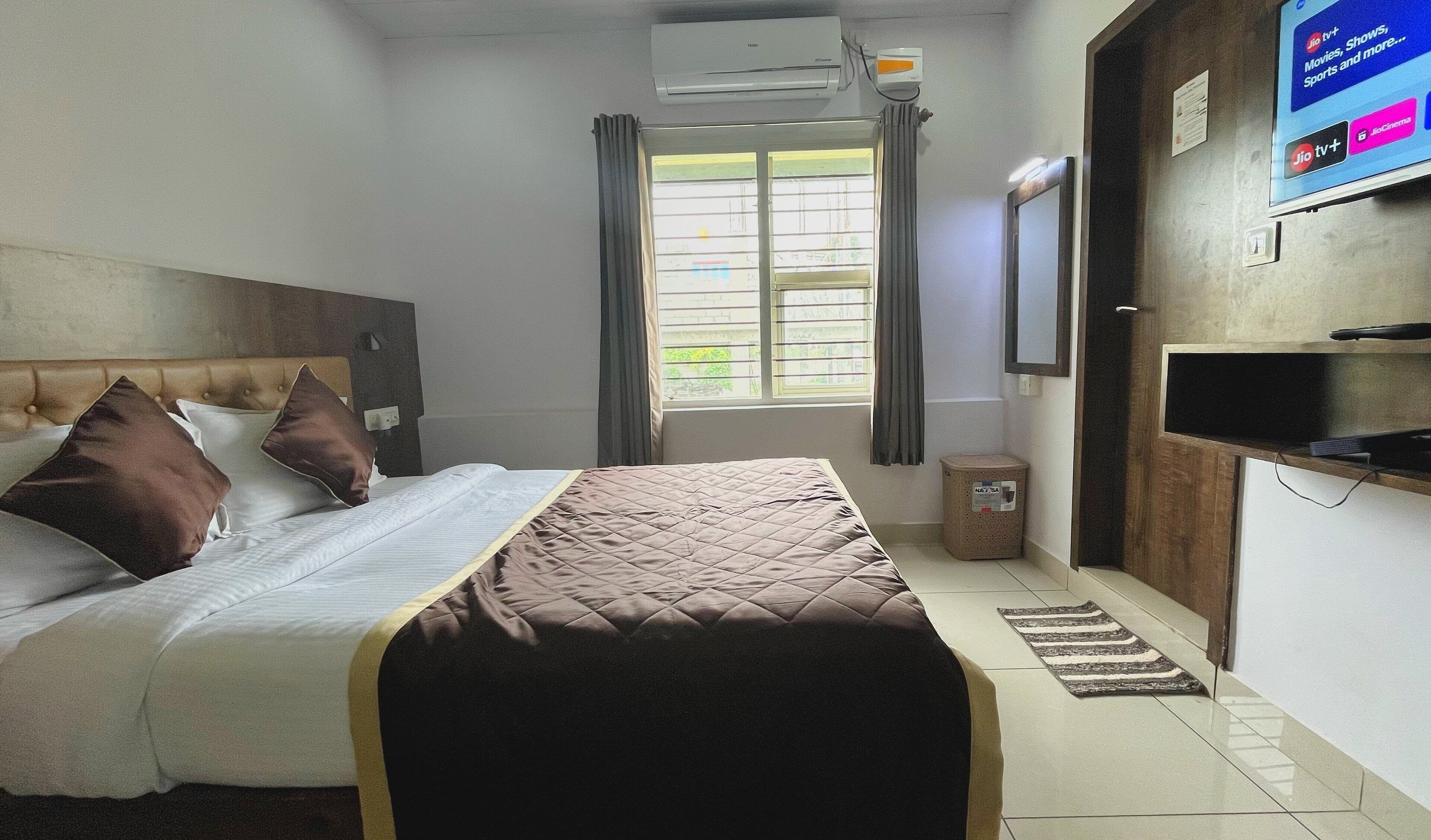 Habitación de hotel con cama, televisor, aire acondicionado, ventana con cortinas y una mesita.