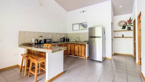 A modern kitchen with a central island, wooden stools, a stainless steel refrigerator, and a ceiling fan. - Complete house in the privacy of a spacious tropical setting (Puerto Jiménez)