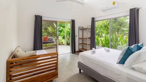 A modern hotel room with a large bed, a wooden bench, a small table, and a balcony with a view of greenery. - Complete house in the privacy of a spacious tropical setting (Puerto Jiménez)