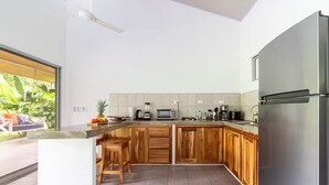 A modern kitchen with wooden cabinets, a stainless steel refrigerator, and a built-in island with stools. - Complete house in the privacy of a spacious tropical setting (Puerto Jiménez)