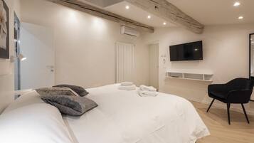 Une chambre à coucher moderne avec un grand lit, un téléviseur à écran plat fixé au mur et une chaise noire.