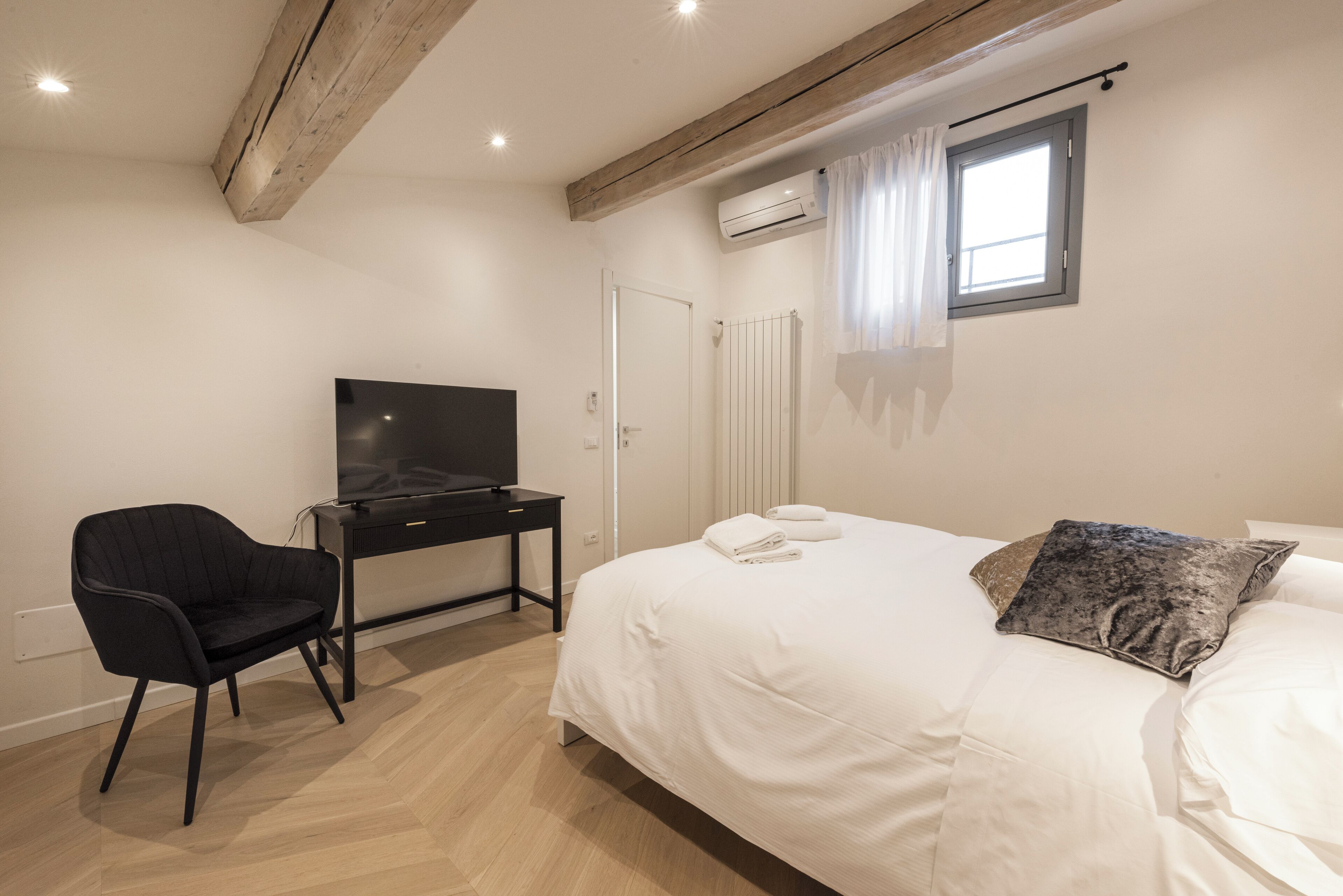 Un dormitorio con cama, escritorio, silla, televisor y aire acondicionado.