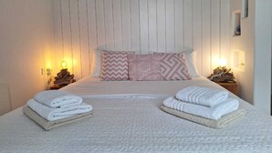 Una cama bien hecha con toallas dobladas, una almohada estampada y una lámpara fijada a la pared.