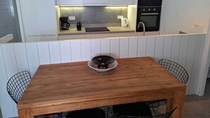 Una cocina moderna con armarios blancos, un horno negro y una mesa de comedor de madera con un tazón encima.