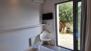 Un dormitorio moderno con cama, una silla blanca, un televisor y una puerta corrediza de vidrio que da a un jardín.
