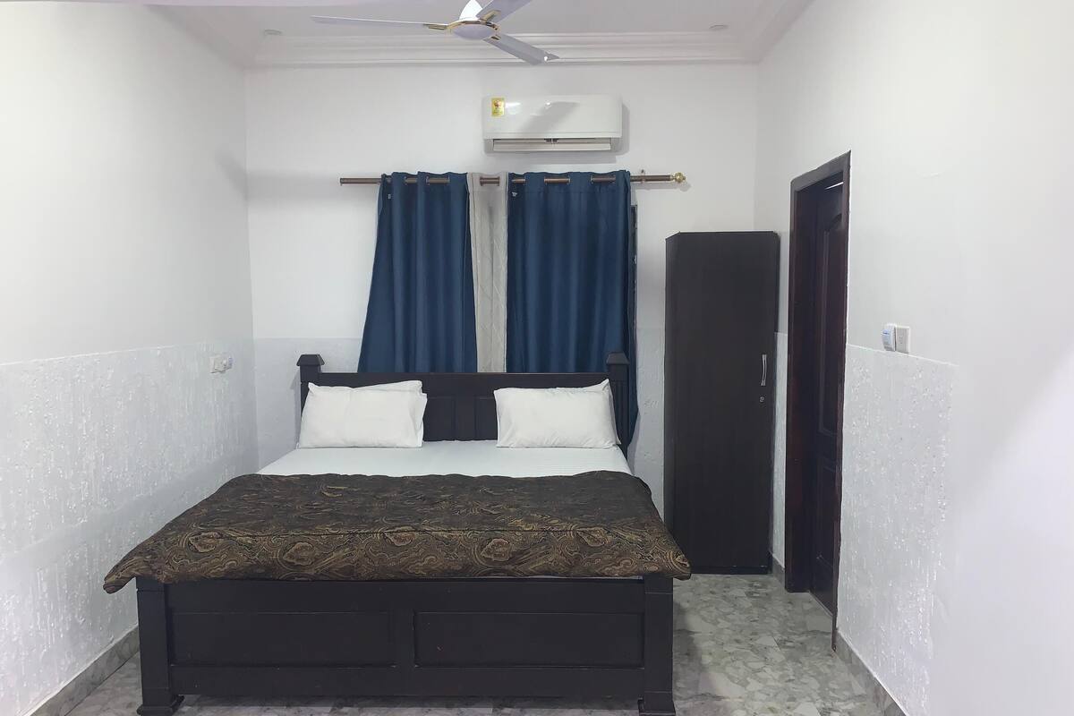 A small, narrow room with a bed, an air conditioning unit, and a door.
