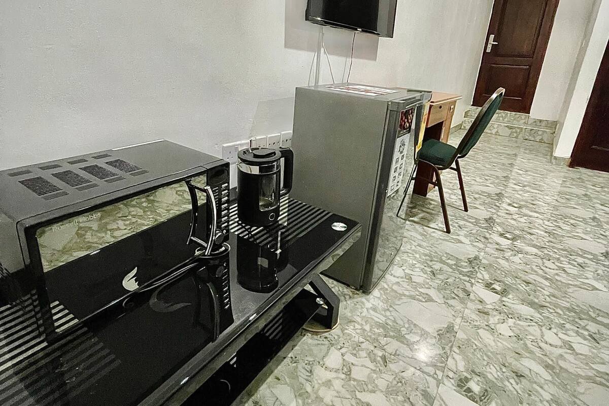 A modern living room with a flat-screen TV mounted on the wall, a coffee machine, and a seating area with a chair and a sofa.