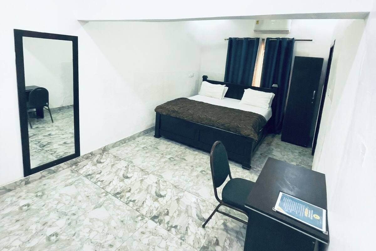 A bedroom with a bed, a desk, a chair, a mirror, and a wardrobe.