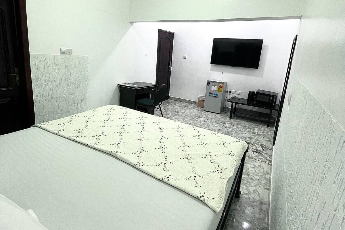 A bedroom with a bed, a desk, a chair, a television, and a microwave.