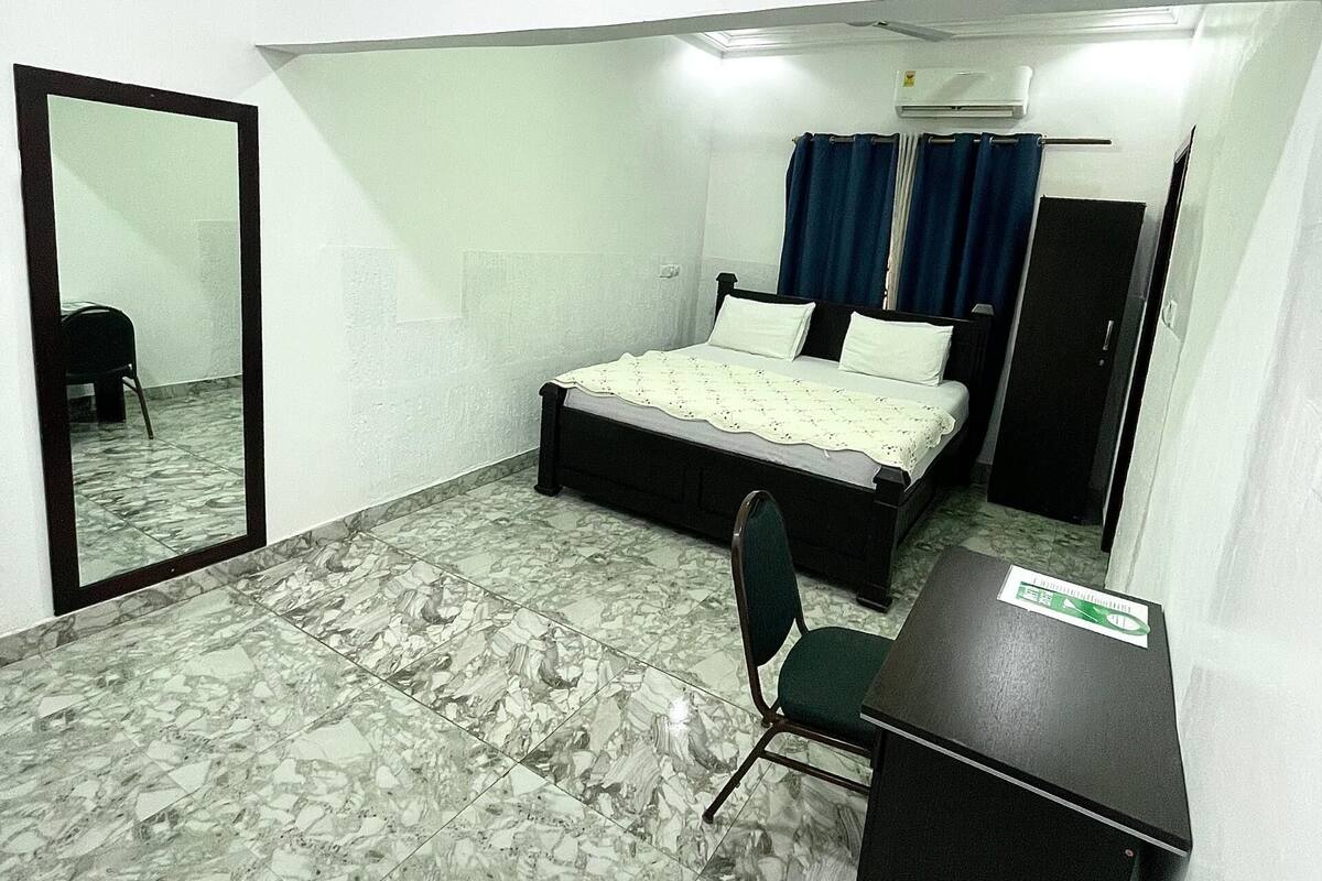 A small, compact room with a bed, a desk, a chair, and a mirror.