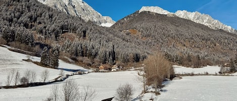 Paisagem montanhosa coberta de neve com um pequeno edifício ao primeiro plano.