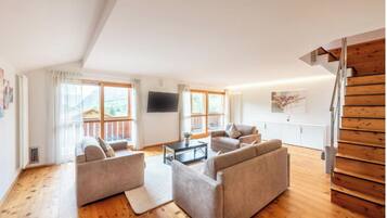 A spacious living room with a wooden floor, two sofas, a coffee table, and a TV mounted on the wall.
