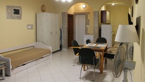 Espaço compacto com cama, mesa de jantar, cadeiras, máquina de lavar e ventilador.