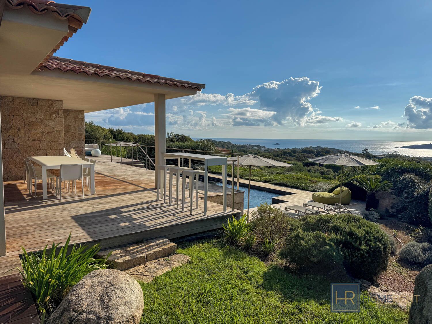 Une terrasse en bois avec des meubles d’extérieur, une piscine et une vue sur la mer.