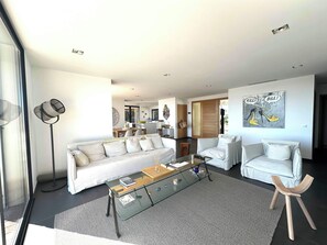 Una sala de estar moderna con un sofá, dos sillones, una mesa de centro de vidrio y una lámpara de pie.
