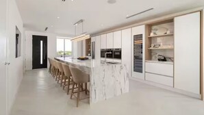 Une cuisine moderne dotée d’un îlot en marbre, de tabourets de bar et d’appareils électroménagers intégrés.