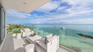 Un balcon moderne avec une balustrade en verre donnant sur une mer bleue et limpide, et sur un bateau.
