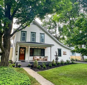 A two-story house with a front porch, a large tree, and a well-maintained lawn.