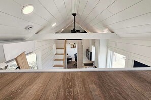 A high-ceilinged room with a wooden floor, a staircase leading to an upper level, and a view of a kitchen area. - Newly built Tiny house on ranch setting in the middle of Scottsdale! (Scottsdale)