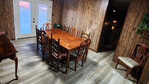 Une salle à manger avec une table et des chaises en bois, un plancher en bois et une vue à travers les portes vitrées.