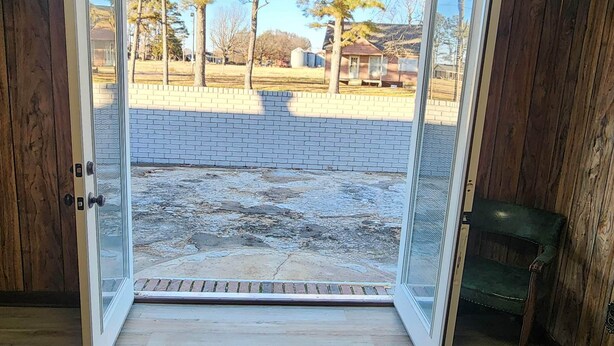 Une pièce dotée d’un plancher en bois et d’une porte-fenêtre coulissante donnant sur un espace extérieur agrémenté d’un mur en briques et d’arbres.