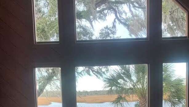 Une pièce dotée de grandes fenêtres donnant sur une terrasse en bois et sur l’eau.