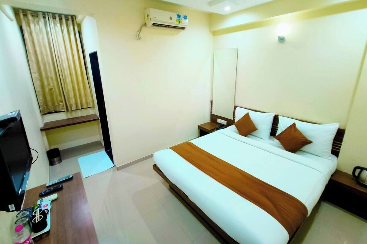 Quarto de hotel com cama, televisão, escrivaninha com controles remotos, espelho e aparelho de ar condicionado.