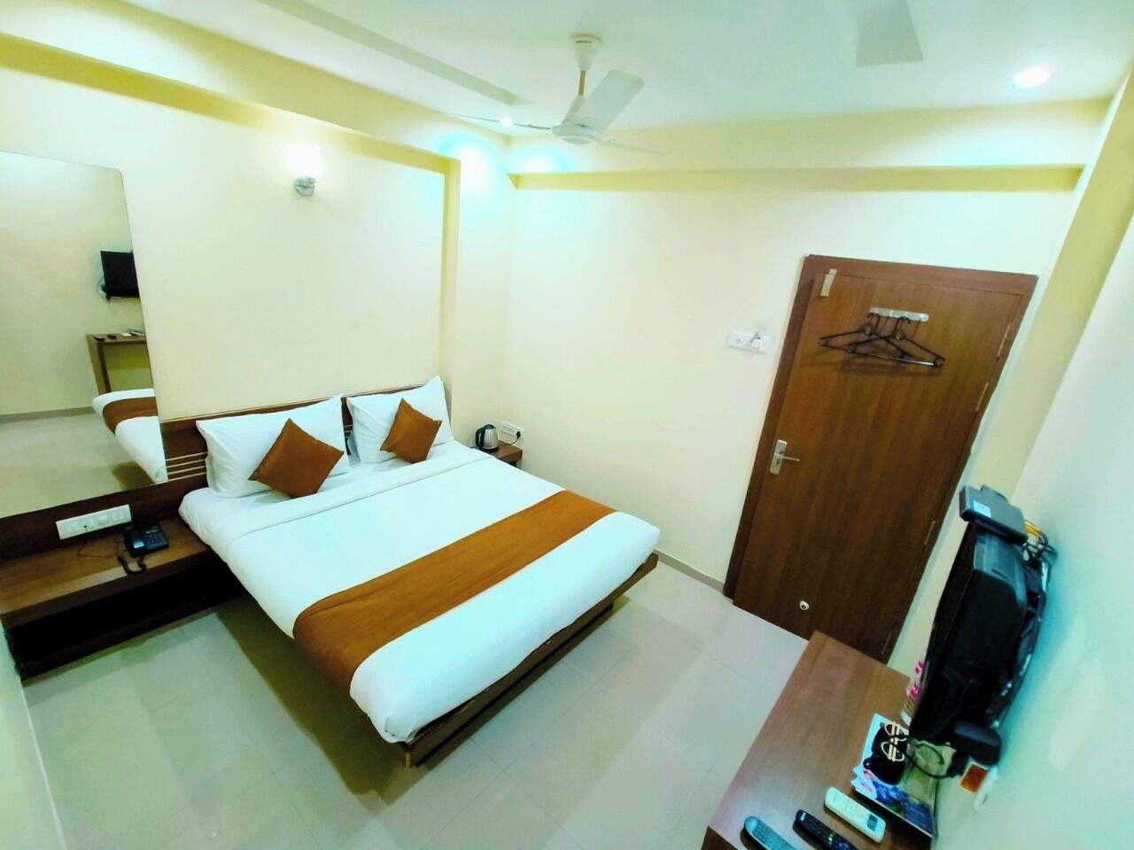 Una habitación de hotel con cama, mesita de noche, espejo, armario y televisor.
