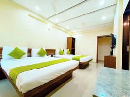 Habitación de hotel con dos camas, cada una con ropa blanca y almohadas verdes, cabecera de madera, televisor de pantalla plana sobre un soporte de madera y encimera de mármol.
