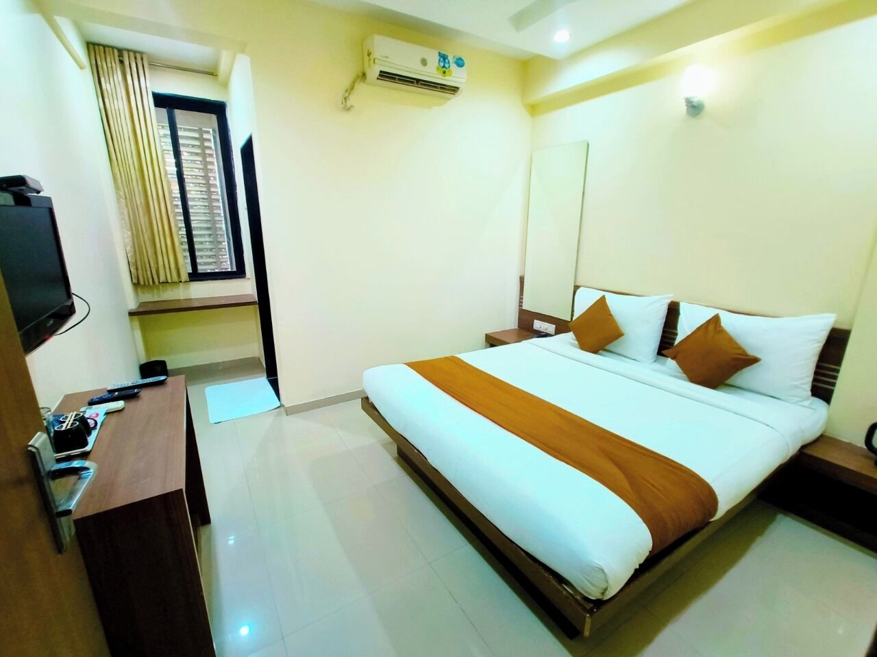 Una habitación de hotel con cama, escritorio, silla, aire acondicionado y ventana con cortinas.