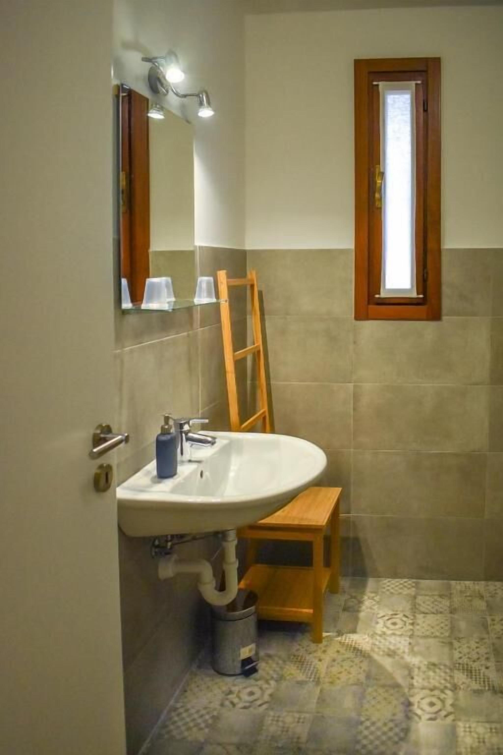 Une salle de bain avec un lavabo blanc, une échelle en bois et une fenêtre avec un cadre en bois.