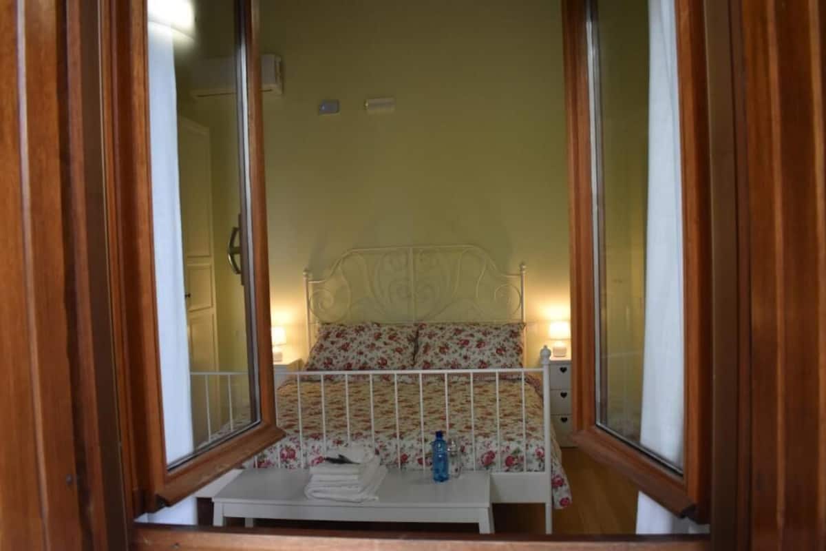 A bedroom with a bed, bedside table, and a window with curtains.